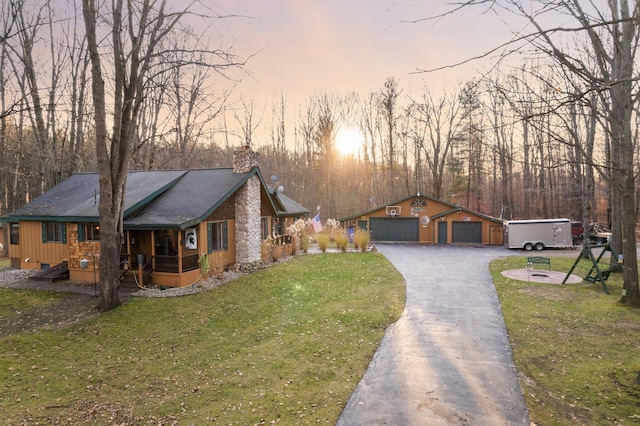 view of front of property featuring a chimney, a yard, a garage, an outbuilding, and covered porch