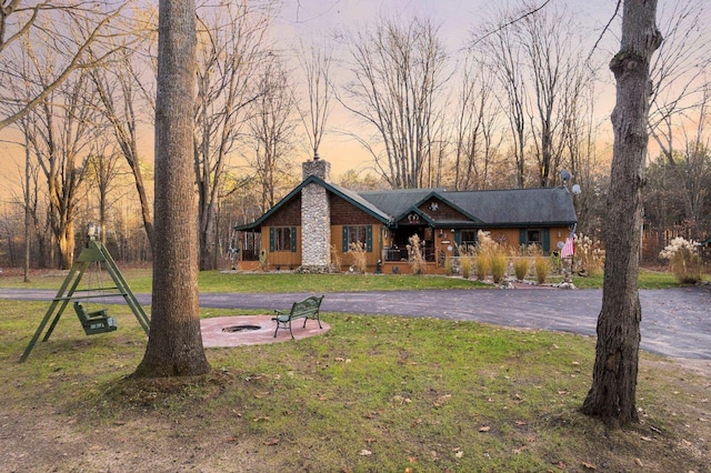 view of front of house featuring a porch, an outdoor fire pit, a chimney, and a front yard