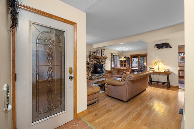 living area with a stone fireplace, baseboards, and light wood finished floors