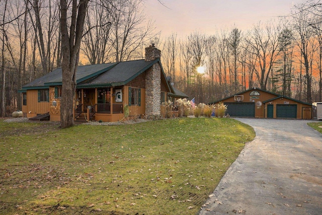 view of front of home featuring covered porch, a chimney, a yard, driveway, and an outbuilding