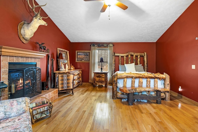 bedroom featuring wood-type flooring, lofted ceiling, a tile fireplace, and ceiling fan