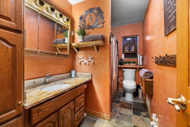 bathroom featuring toilet, stone tile flooring, baseboards, vanity, and curtained shower