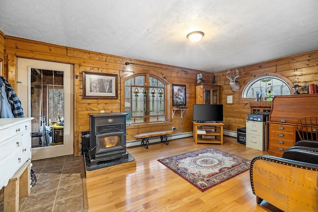 living room with wooden walls, a wood stove, a textured ceiling, baseboard heating, and wood finished floors
