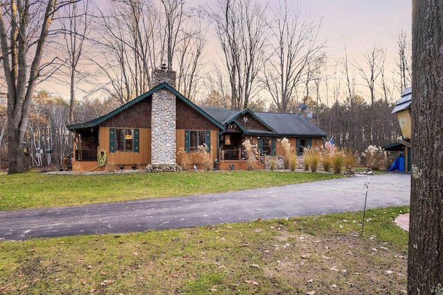 view of front of home with a porch, a chimney, a front yard, and asphalt driveway