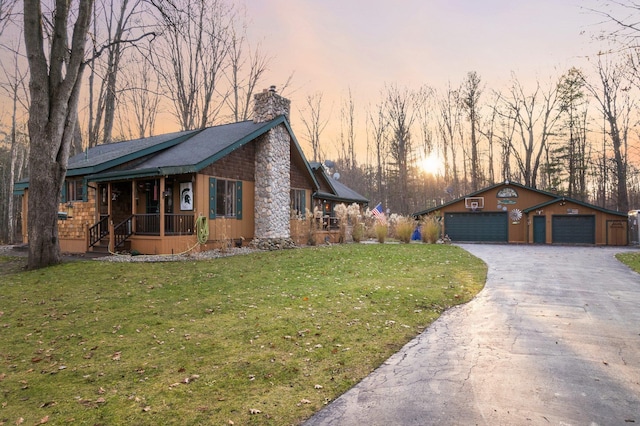 view of front of home featuring a porch, a chimney, a lawn, a detached garage, and driveway