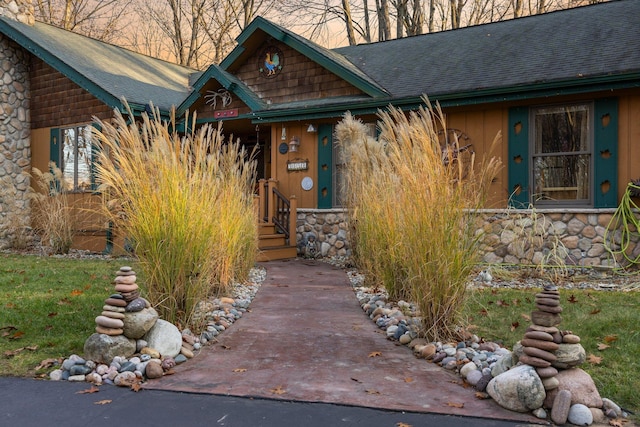 view of exterior entry featuring a shingled roof and stone siding
