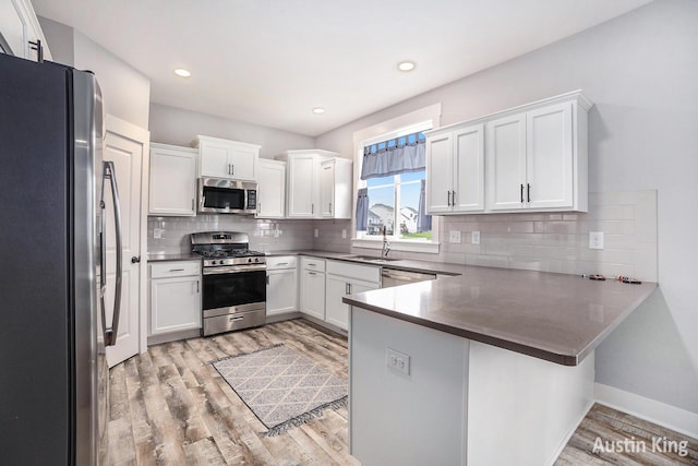 6526 Alward Dr, Hudsonville, MI 49426 - kitchen featuring appliances with stainless steel finishes, a peninsula, a sink, light wood-style flooring, and white cabinets