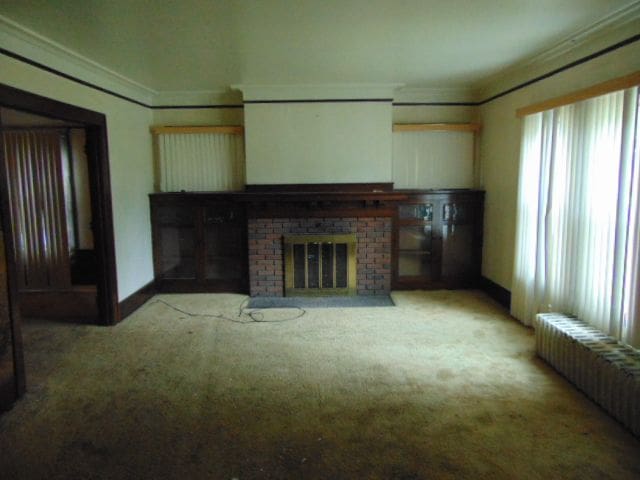 50 Glendale St, Highland Park, MI 48203 - unfurnished living room featuring radiator, ornamental molding, carpet flooring, and a brick fireplace
