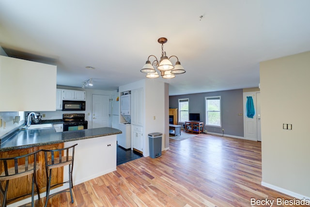 823 Warner St, Whitehall, MI 49461 - kitchen with black appliances, stacked washing machine and dryer, a sink, dark countertops, and a peninsula