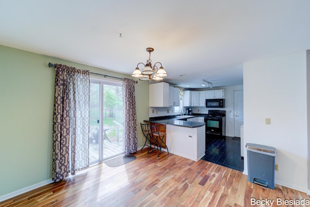 823 Warner St, Whitehall, MI 49461 - kitchen with black appliances, a peninsula, a sink, a chandelier, and light wood-style flooring