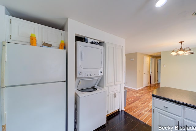 823 Warner St, Whitehall, MI 49461 - laundry room featuring stacked washer / drying machine, dark wood-style flooring, a chandelier, and baseboards