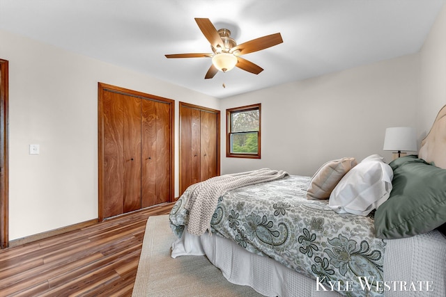 bedroom with two closets, wood finished floors, ceiling fan, and baseboards