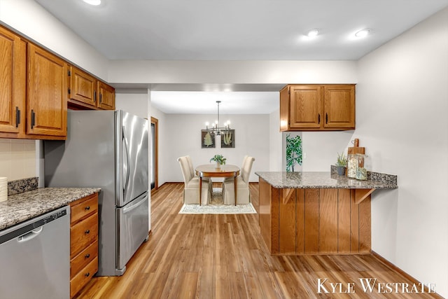 kitchen with appliances with stainless steel finishes, brown cabinetry, light wood-style floors, a peninsula, and stone counters