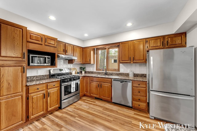 kitchen with appliances with stainless steel finishes, a sink, brown cabinetry, under cabinet range hood, and recessed lighting