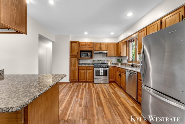 kitchen featuring stainless steel appliances, a sink, brown cabinetry, light wood-type flooring, and under cabinet range hood