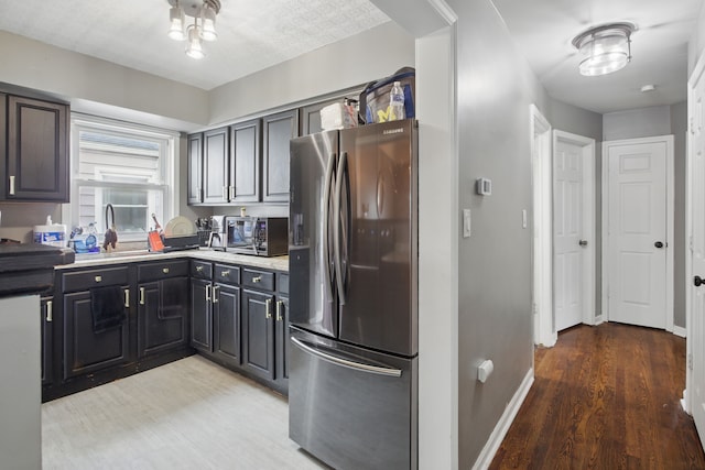 kitchen featuring stainless steel appliances, light wood-style floors, a sink, light countertops, and baseboards