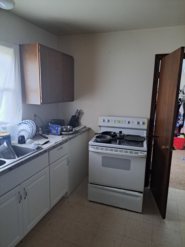 kitchen with white electric range oven, white cabinets, and a sink