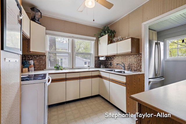 kitchen featuring a sink, freestanding refrigerator, white electric stove, wallpapered walls, and light countertops
