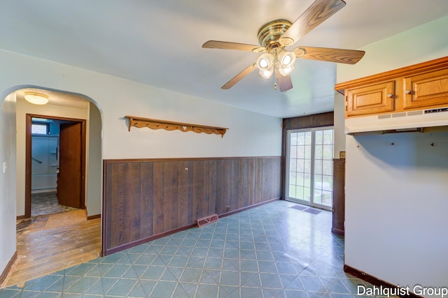 kitchen with under cabinet range hood, ceiling fan, arched walkways, tile patterned floors, and baseboards
