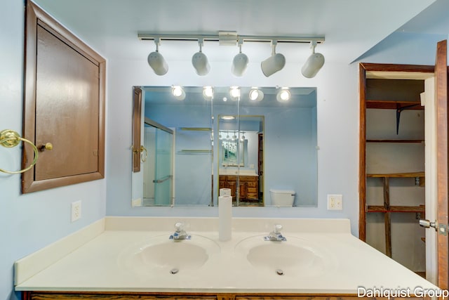 bathroom with double vanity, a shower with door, and toilet