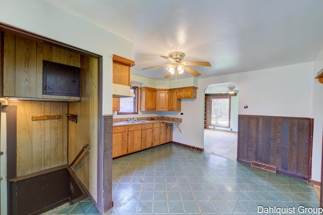 kitchen with a ceiling fan, light flooring, brown cabinets, a sink, and arched walkways