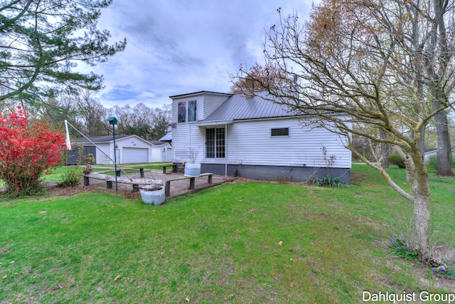 rear view of house featuring a detached garage, a lawn, and metal roof