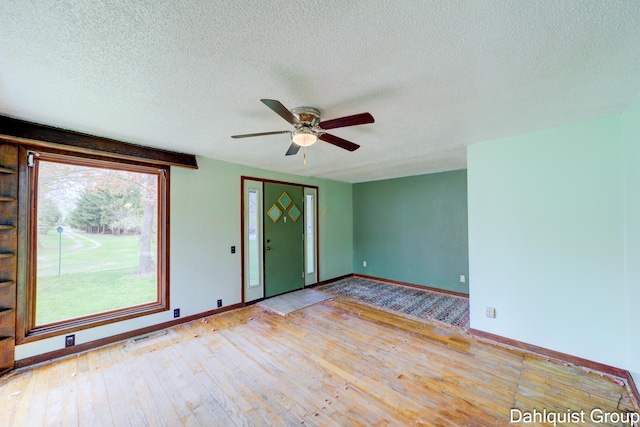 empty room with hardwood / wood-style floors, a ceiling fan, a textured ceiling, and baseboards