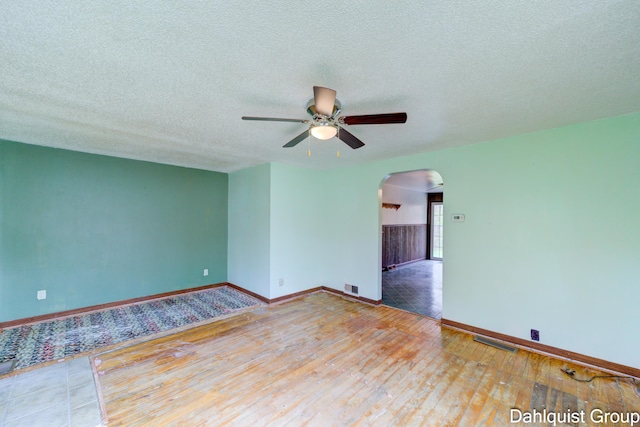 spare room with arched walkways, wood-type flooring, ceiling fan, baseboards, and a textured ceiling