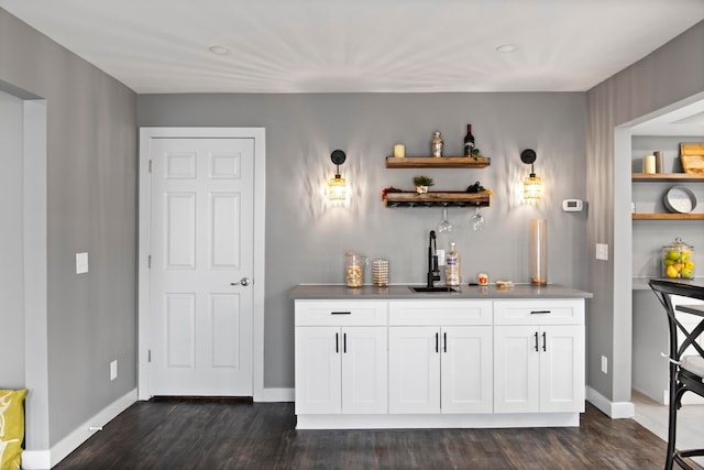 indoor wet bar featuring dark wood-style floors and baseboards