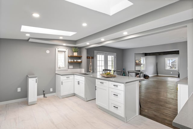 kitchen with a skylight, recessed lighting, a sink, a peninsula, and white cabinetry