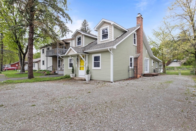 view of front of home featuring a balcony, a shingled roof, and a chimney