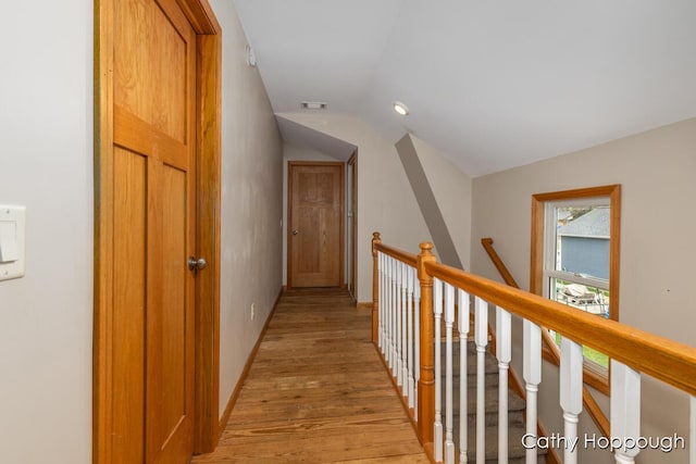 corridor featuring vaulted ceiling, light wood-style flooring, an upstairs landing, and baseboards
