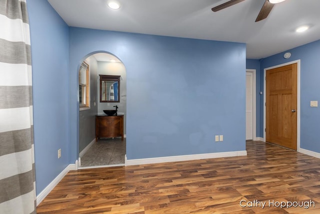 spare room with wood finished floors, a ceiling fan, arched walkways, baseboards, and recessed lighting