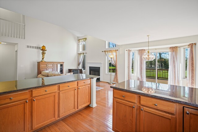 kitchen featuring light wood-style flooring, a fireplace, hanging light fixtures, dark stone counters, and lofted ceiling