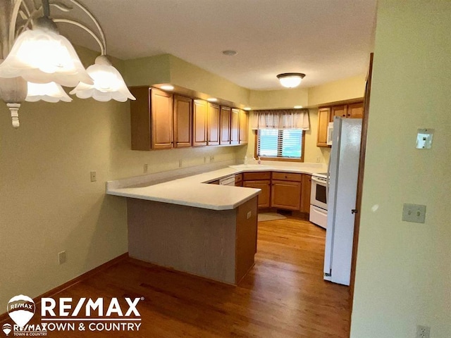 kitchen featuring a peninsula, white appliances, light wood-style floors, light countertops, and a sink