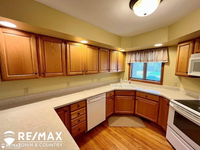 kitchen with white appliances, a sink, light countertops, and light wood-type flooring