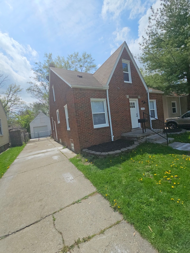 view of front of house with brick siding, a front lawn, a detached garage, driveway, and an outbuilding