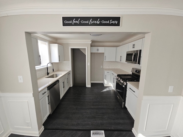 kitchen featuring stainless steel appliances, a sink, light countertops, decorative backsplash, and crown molding