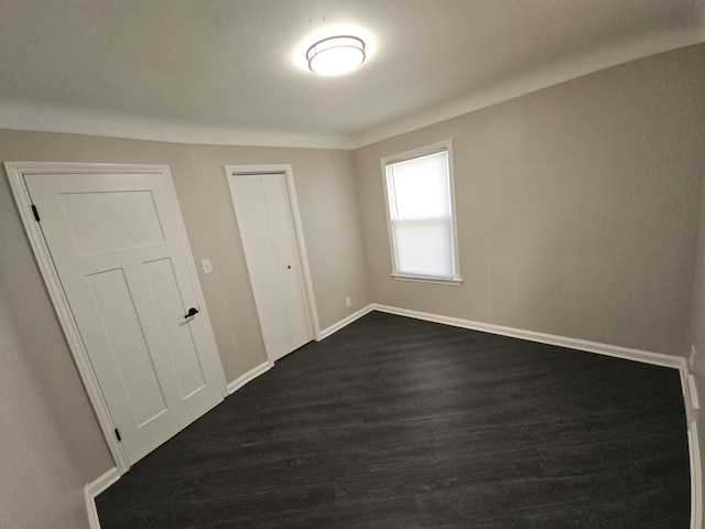 unfurnished bedroom featuring dark wood finished floors, baseboards, and a closet