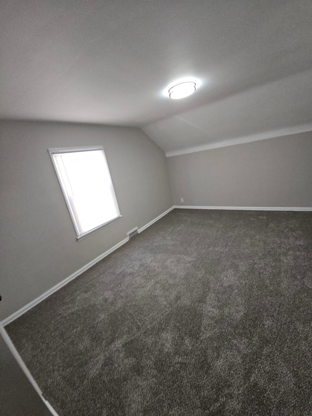 bonus room with vaulted ceiling, dark carpet, and baseboards