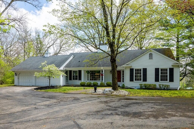 single story home with asphalt driveway, an attached garage, roof with shingles, and a front yard