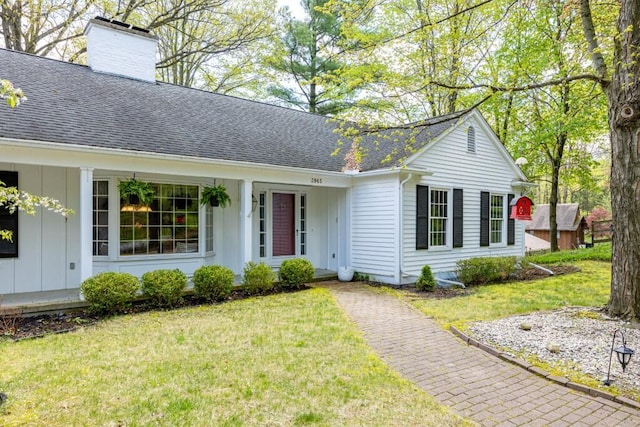 view of front facade with board and batten siding, roof with shingles, a chimney, and a front lawn