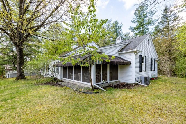 rear view of property with central AC, a chimney, a sunroom, and a lawn