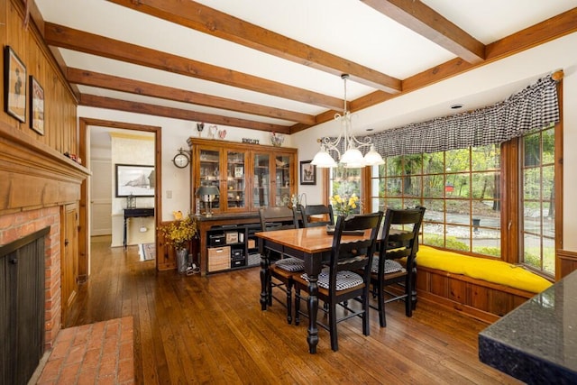 dining space featuring beamed ceiling, dark wood-type flooring, plenty of natural light, a chandelier, and a fireplace