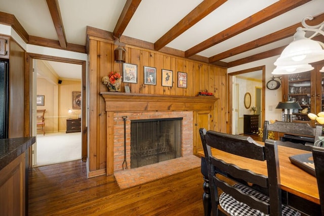 dining area featuring beamed ceiling, dark wood-type flooring, a fireplace, and wooden walls