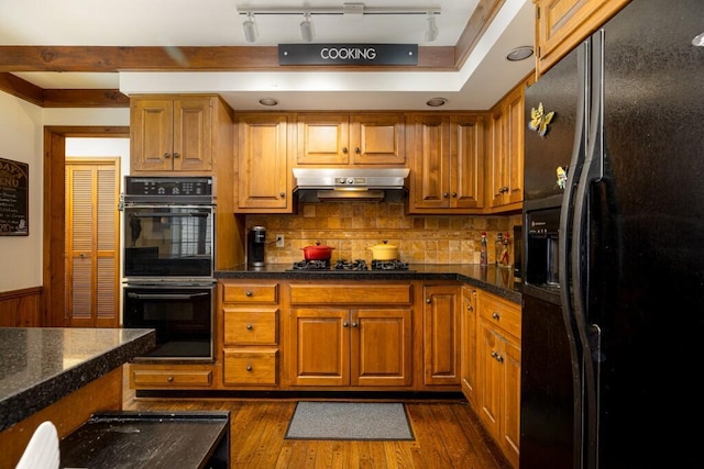kitchen featuring black appliances, under cabinet range hood, brown cabinets, dark wood-style flooring, and decorative backsplash