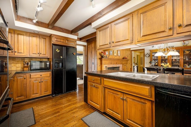 kitchen with black appliances, rail lighting, dark countertops, a sink, and beam ceiling