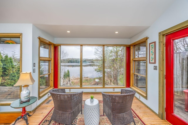 sunroom / solarium with hardwood / wood-style floors, a water view, and recessed lighting