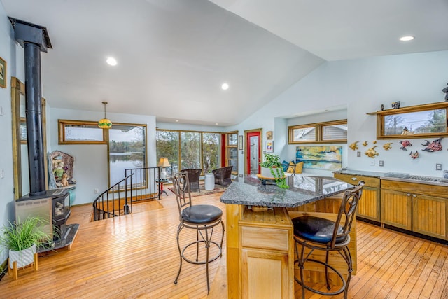 kitchen with a wood stove, light wood finished floors, a breakfast bar area, vaulted ceiling, and a center island