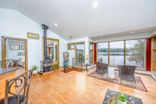 living area with lofted ceiling, hardwood / wood-style flooring, a wood stove, a water view, and recessed lighting